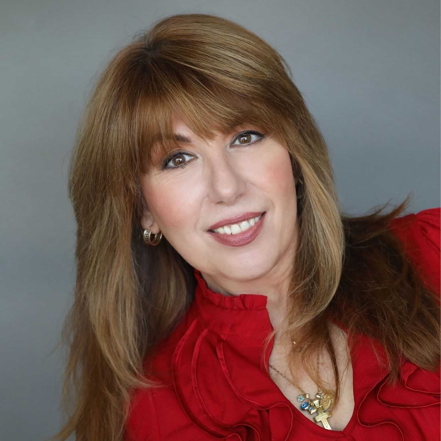 Woman with shoulder-length brown hair smiling, wearing a red blouse and gold necklace.