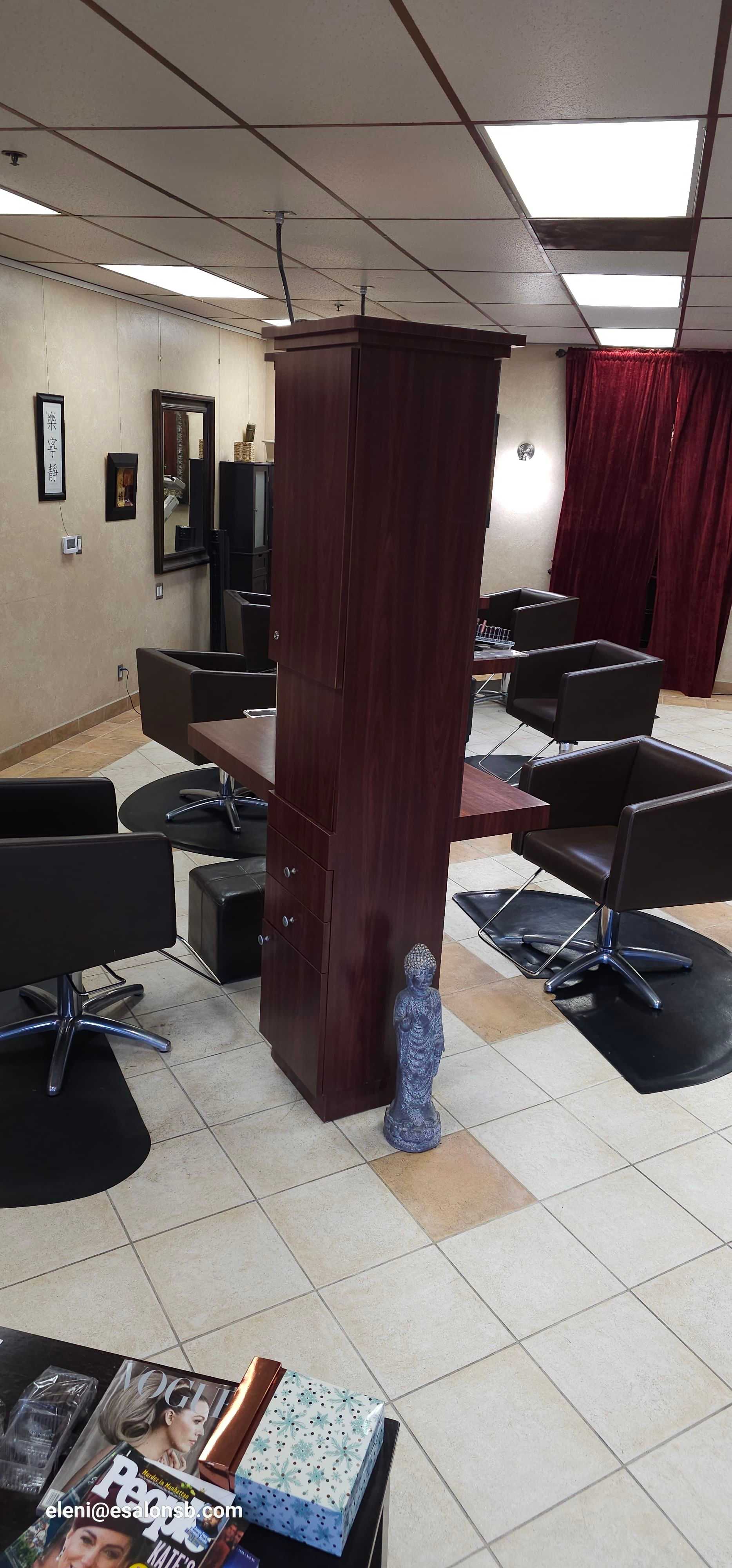 Modern hair salon with black chairs, mirrors, and a central wooden cabinet for supplies.