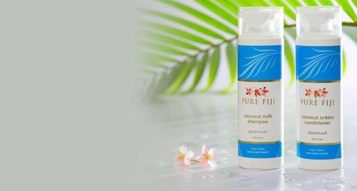 Pure Fiji coconut milk shampoo and conditioner bottles with tropical leaves and flowers in the background.