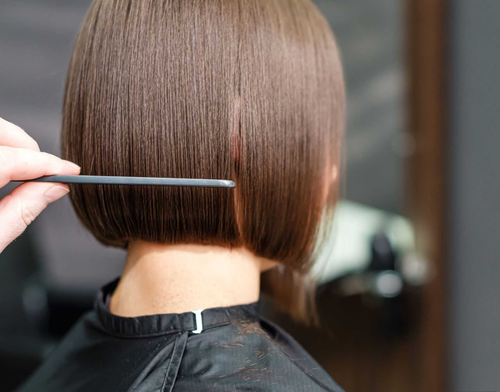 Hairdresser trimming a neat bob haircut with a comb and scissors from the back in a salon.